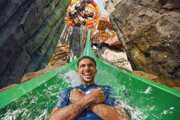 Illuminated water slides and attractions at Yas Waterworld at night, with colorful lights reflecting off the water and excited visitors enjoying the rides